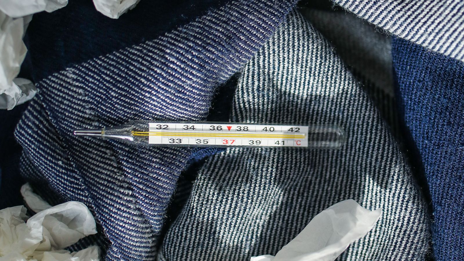 Thermometer surrounded by used tissues, symbolising flu symptoms